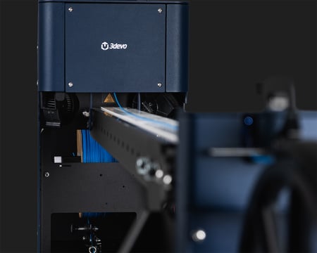 Close-up of the FMX10 extruder head where filament enters the conveyor belt, showing the heat-warning label and cooling fans.