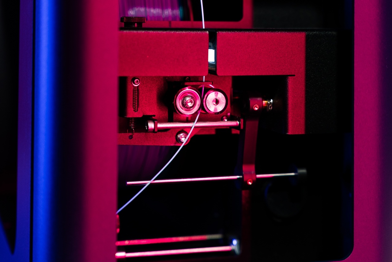 The puller wheels and winder system guiding the light blue filament onto the spool, while maintaining enough tension