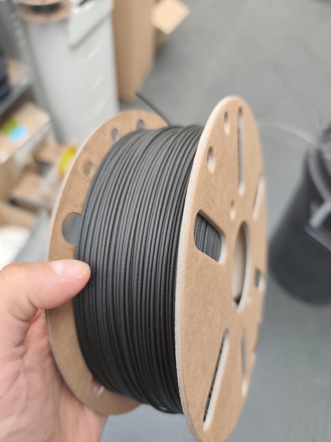 Hand holding a cardboard spool of black rPA12 + 10% rCF filament.
